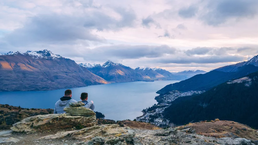 Two people sitting on Queenstown Hill overlooking Lake Wakatipu and the Southern Alps