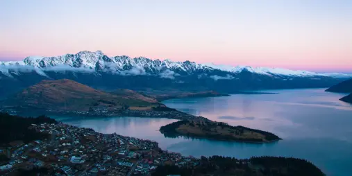 Aerial view of Queenstown and Lake Wakatipu with snow-covered Remarkables mountain range at sunset in winter.