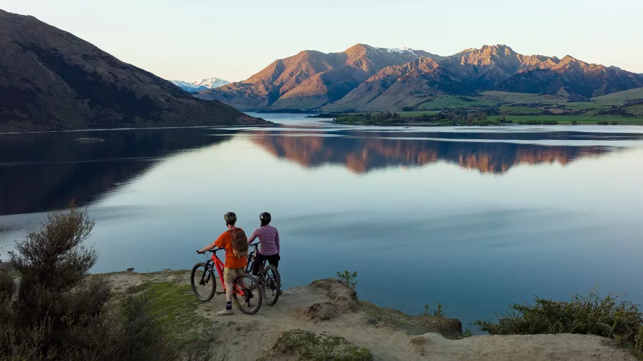 Cyclists pause at Wānaka lakefront with views of mountains and still water