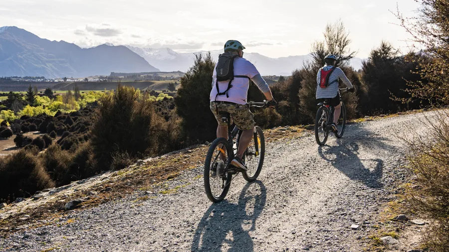 Cyclists ride along Hawea River Track near Wānaka with mountain views