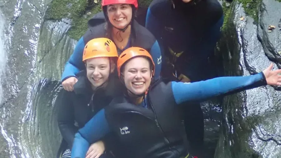 Four smiling canyoners posing together in a rock chute at Niger Stream near Wānaka.