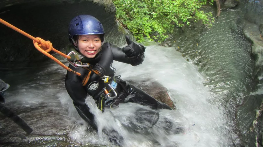 Smiling canyoner gives a thumbs up while sliding down a natural rock chute in Mt Aspiring National Park.