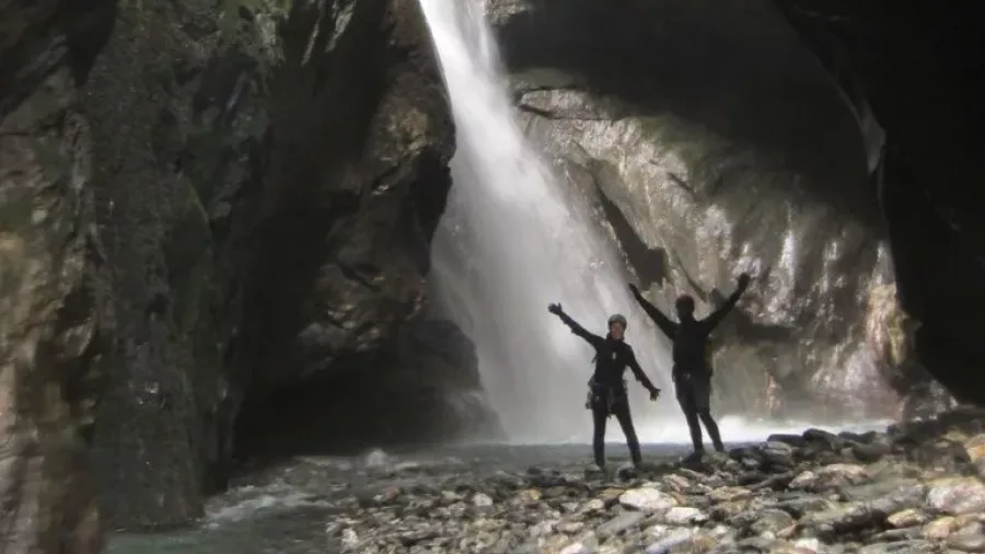 Two canyoners standing in front of a massive cavern waterfall in Robinson Creek near Wānaka.