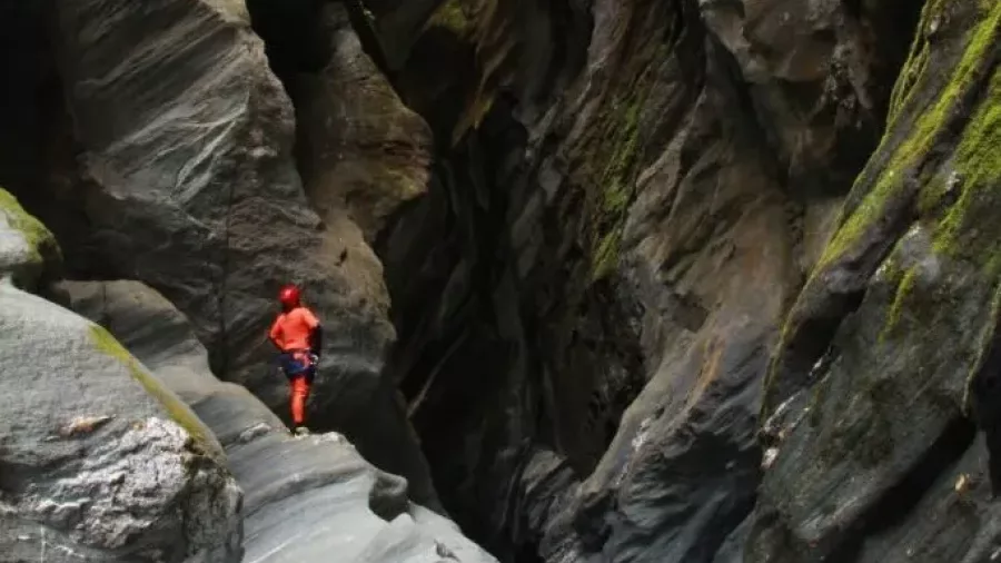 Canyoner walking through narrow gorge walls in Mill Creek Canyon near Wānaka.