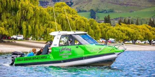 Green self-drive powerboat from Lakeland Wanaka cruising near the shore of Lake Wanaka.