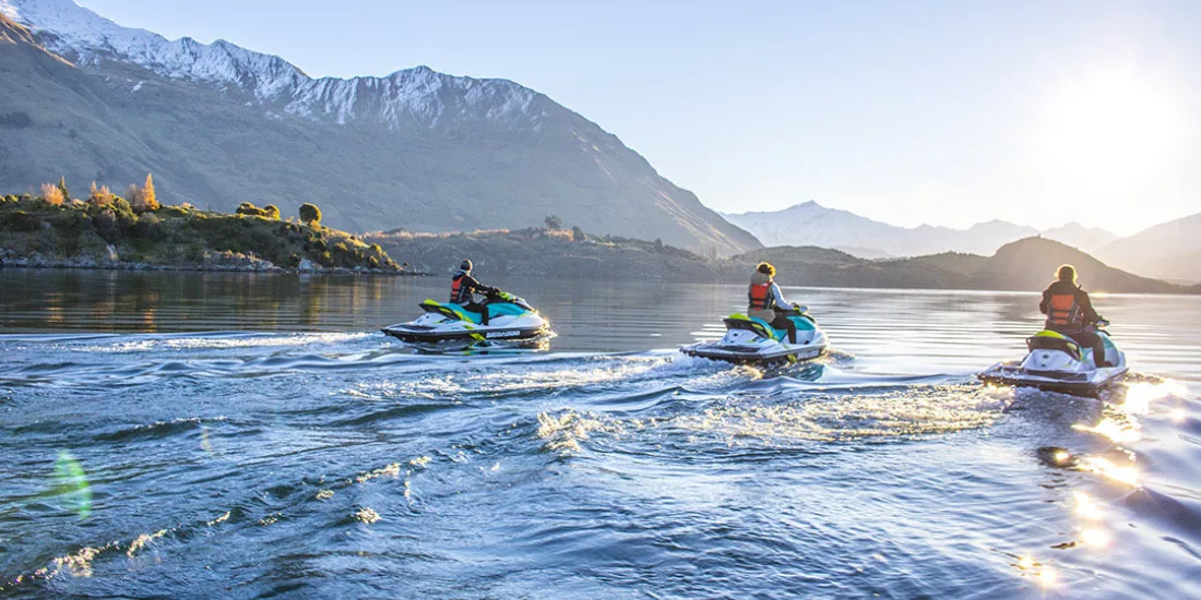 Three people riding jet skis together on Lake Wanaka at sunrise with snow-capped peaks.