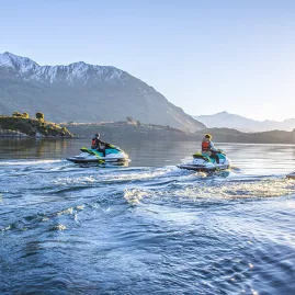 Three people riding jet skis together on Lake Wanaka at sunrise with snow-capped peaks.