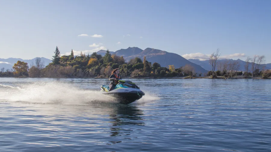 Jet ski rider cruising past Ruby Island on Lake Wanaka with mountains in the background.