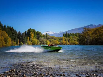 Lakeland jet boat skimming across Lake Wanaka with Fog Peak and autumn trees in the background.