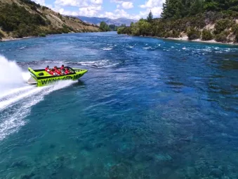 Aerial view of a green jet boat carving through the turquoise waters of the Clutha River near Lake Wanaka.