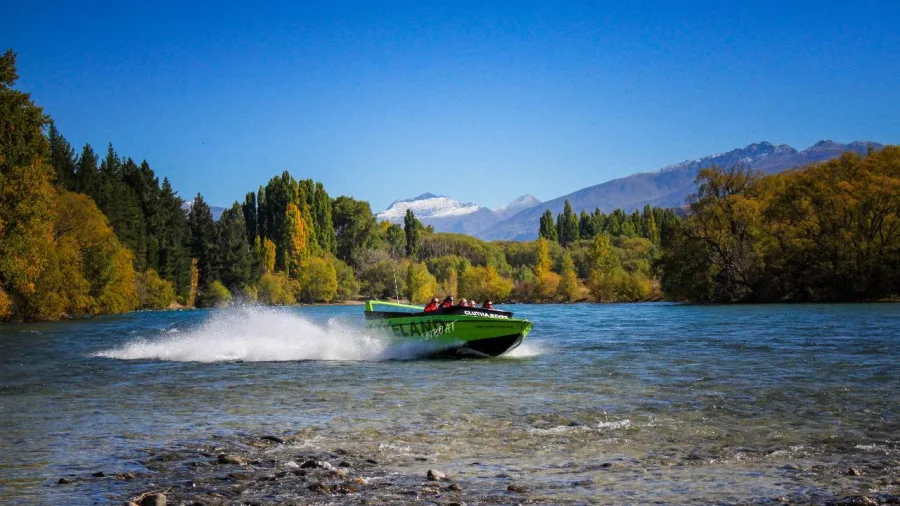 Lakeland jet boat skimming across Lake Wanaka with Fog Peak and autumn trees in the background.