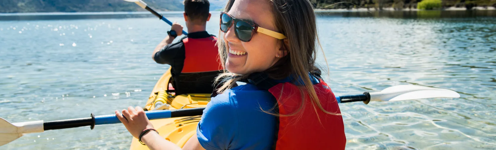 Smiling woman kayaking on Lake Wanaka during a double kayak rental with Paddle Wanaka.