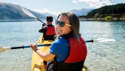 Smiling woman kayaking on Lake Wanaka during a double kayak rental with Paddle Wanaka.
