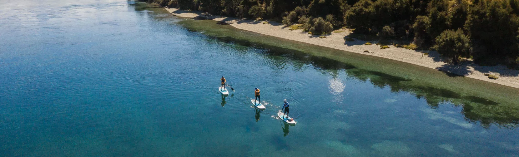 Paddle boarders gliding on calm waters near the Lake Wanaka shoreline