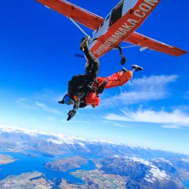 Skydiver jumping from a Skydive Wanaka aircraft with Lake Wanaka in the background