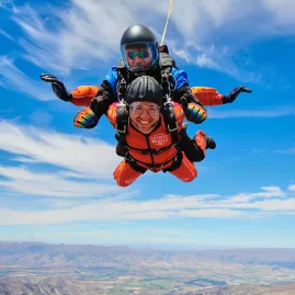 Tandem skydiver with instructor smiling mid-air above Otago landscape