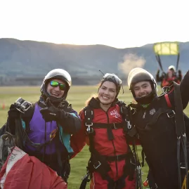 Happy group of tandem skydivers smiling after landing near Wanaka with parachute in background