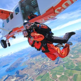 Tandem pair jumping from Skydive Wanaka plane with rivers and lakes far below