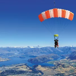 Tandem skydivers exiting orange Skydive Wanaka plane above thick cloud layer