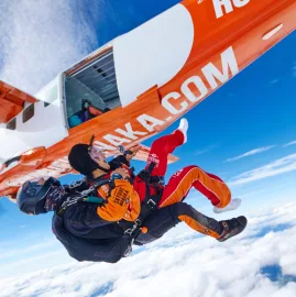 Tandem skydivers exiting orange Skydive Wanaka plane above the clouds