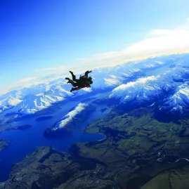 Tandem skydivers freefalling above Lake Wanaka and snow-covered Southern Alps