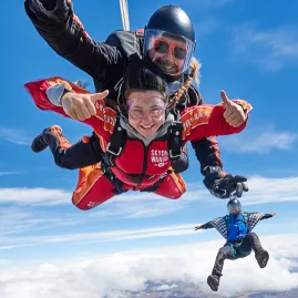 Tandem skydivers giving thumbs up with another jumper mid-air in the background