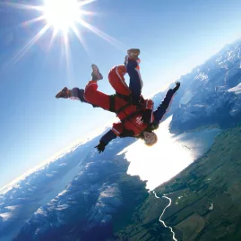 Tandem skydive with bright sun overhead and view of lakes and snow-capped peaks