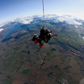 Tandem skydivers descending with parachute over Otago’s green farmland