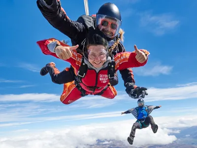 Tandem skydivers giving thumbs up with another jumper mid-air in the background