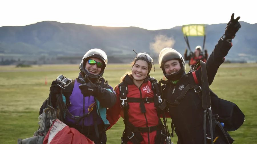 Happy group of tandem skydivers smiling after landing near Wanaka with parachute in background