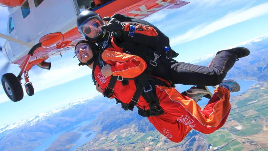 Tandem pair jumping from Skydive Wanaka plane with rivers and lakes far below