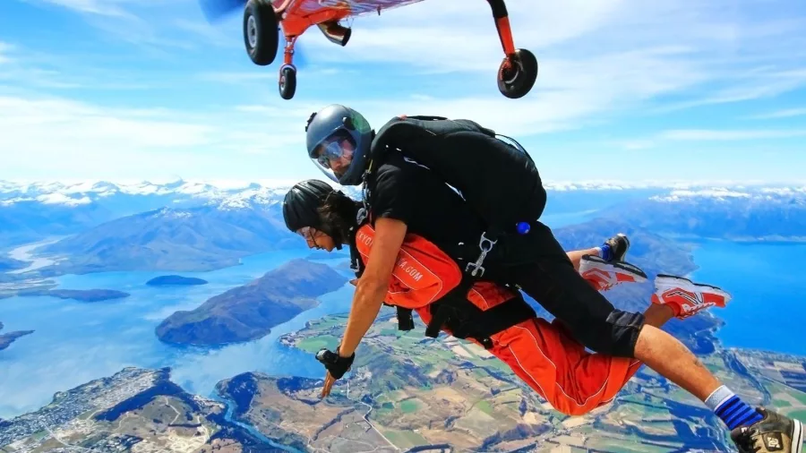 Skydivers leaping from plane with aerial view of farmland and Lake Wanaka in distance