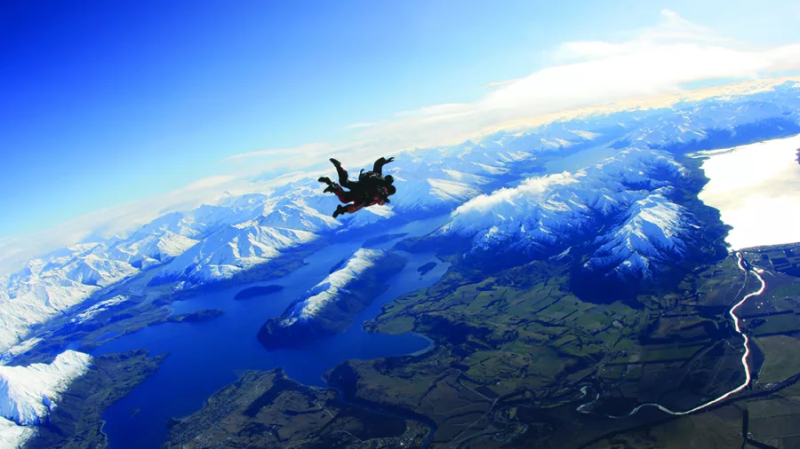 Tandem skydivers freefalling above Lake Wanaka and snow-covered Southern Alps