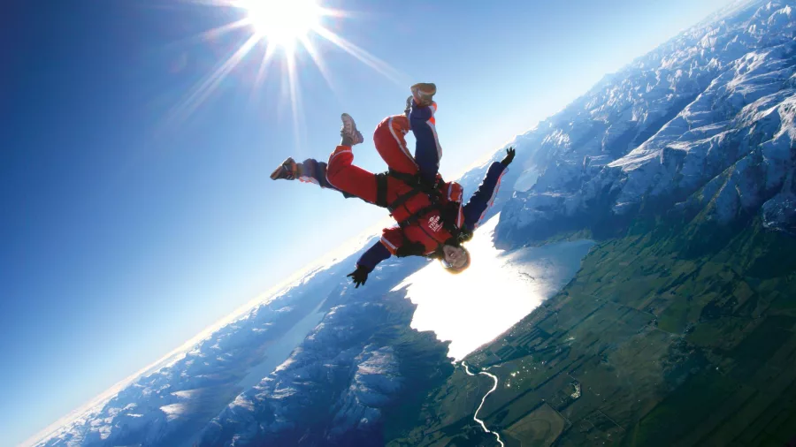 Tandem skydive with bright sun overhead and view of lakes and snow-capped peaks