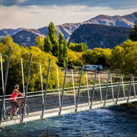 Cyclist in red shirt riding across suspension bridge on Hawea River Trail