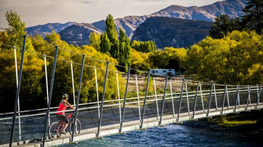 Cyclist in red shirt riding across suspension bridge on Hawea River Trail