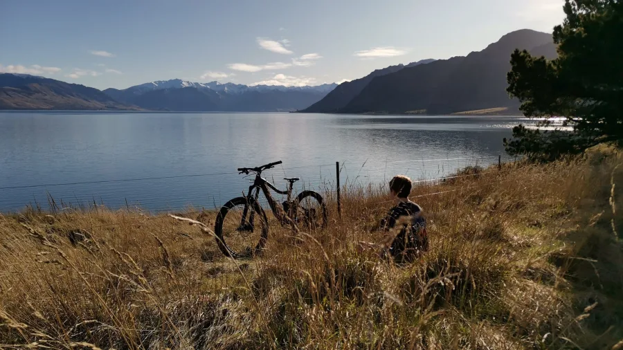 Cyclist resting in grass overlooking Lake Hawea with bike