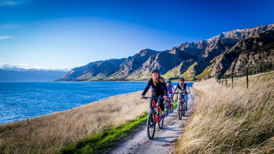 Family cycling beside Lake Hawea with mountains in distance