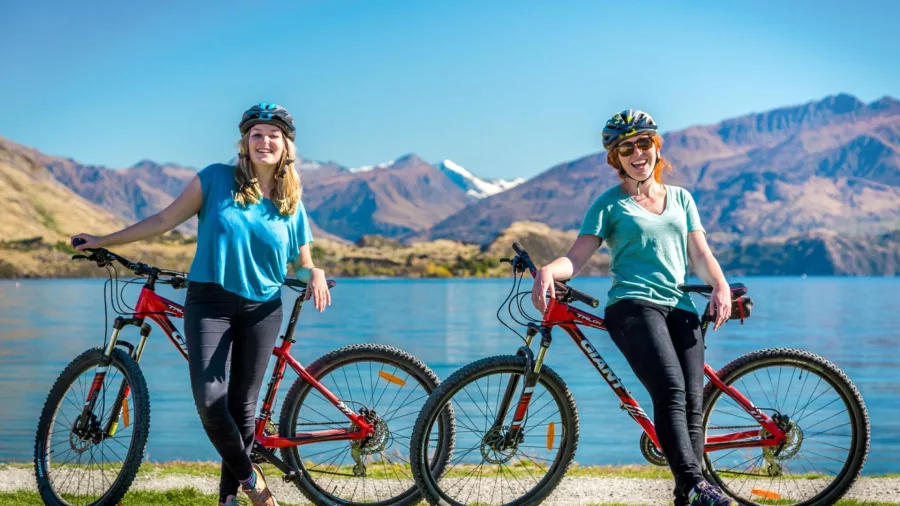 Two cyclists posing by Lake Wanaka after completing the trail