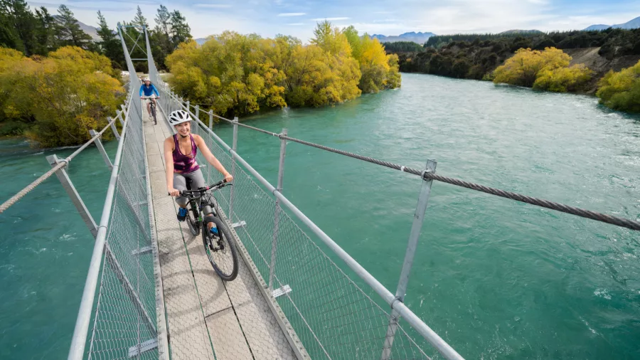 Cyclist riding across suspension bridge over Hawea River