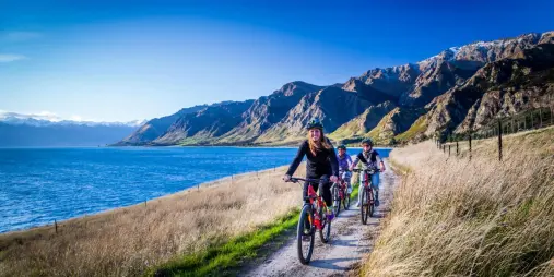 Family cycling beside Lake Hawea with mountains in distance