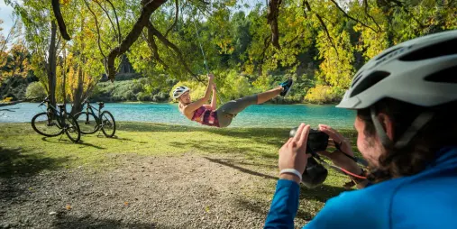 Cyclist swinging from tree beside Hawea River on Lake Hawea to Wanaka bike trail