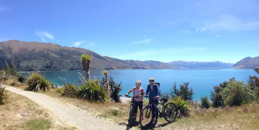 Two cyclists overlooking Lake Hawea with mountains in background