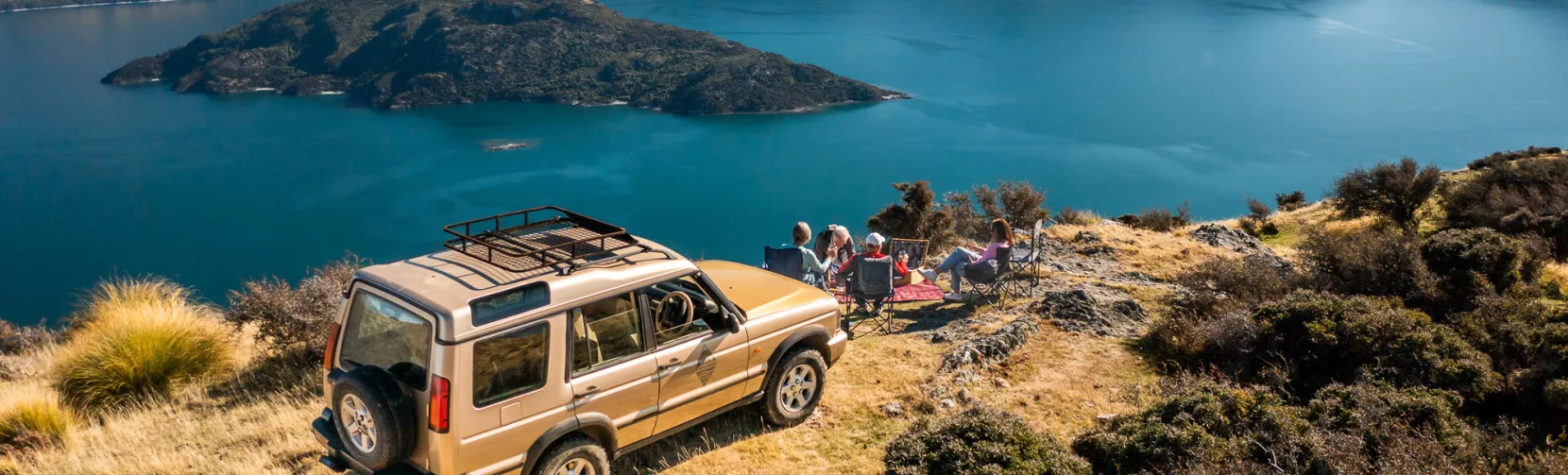 4WD parked on a hill with group enjoying panoramic views of Lake Wanaka and Stevenson’s Island.