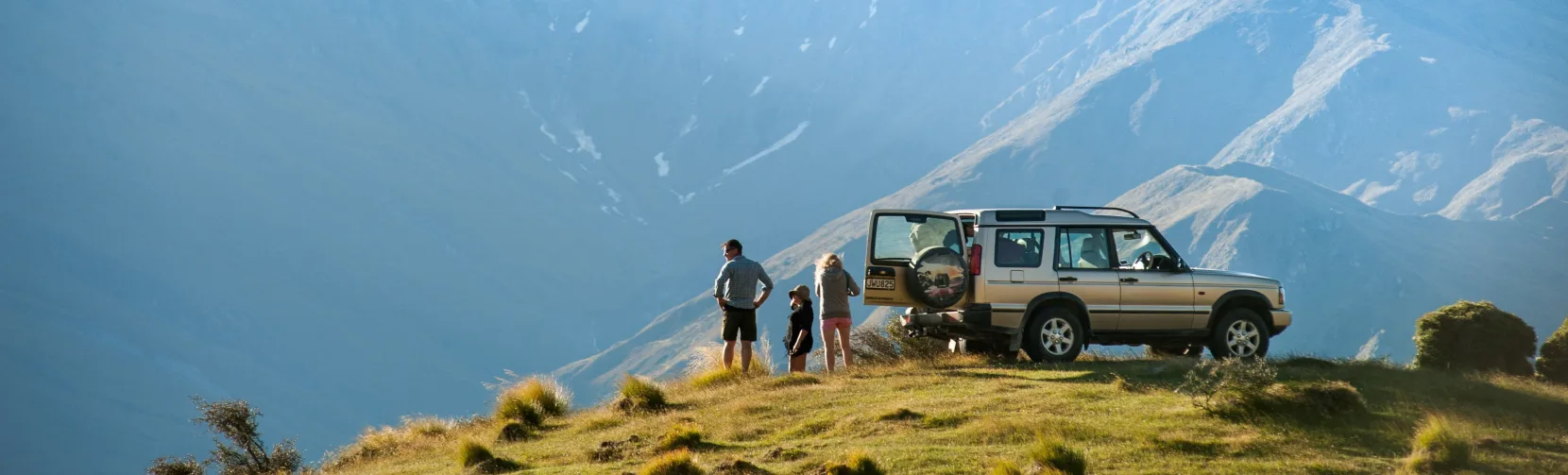 A 4WD vehicle parked on a ridge with people admiring the view of Mount Aspiring in the background.