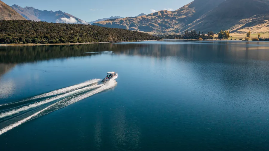 A water taxi cruising across the calm waters of Lake Wanaka with mountain reflections.