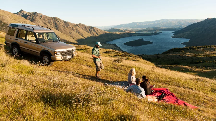 A picnic set up on a hillside with a 4WD vehicle and views over Lake Wanaka.