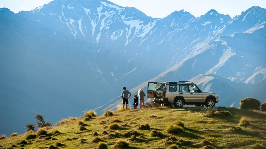 A 4WD vehicle parked on a ridge with people admiring the view of Mount Aspiring in the background.