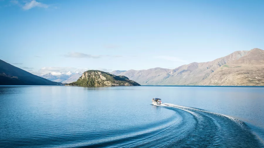 Scenic boat cruising across Lake Wanaka towards Mou Waho Island under clear blue skies