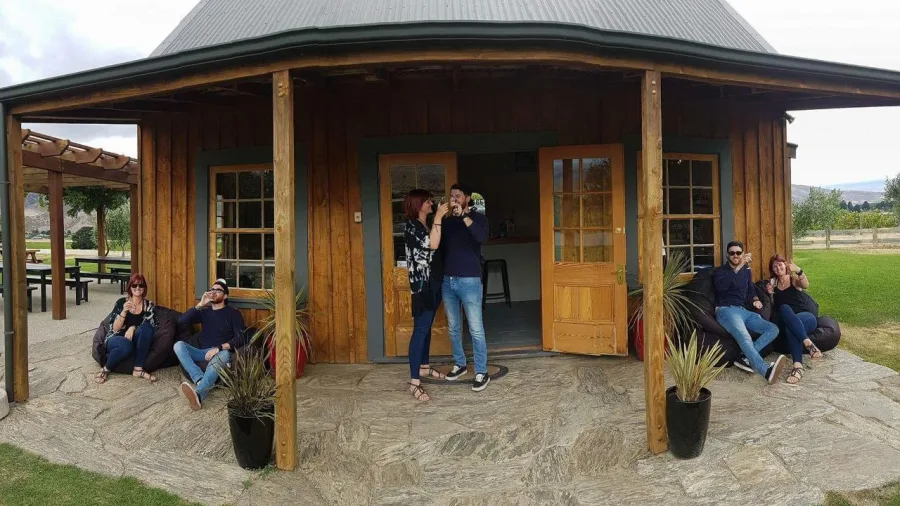 Guests lounging with wine glasses outside the rustic cellar door at Scott Base Wines in Central Otago.
